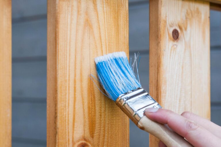 Akazienholz streichen – Hand streicht Holzlatte mit blauem Pinsel