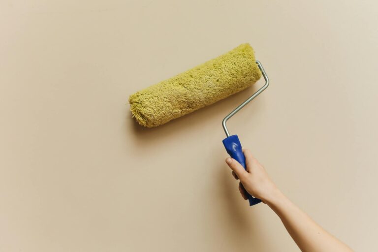 Buntsteinputz streichen – Hand mit gelber Farbrolle an beiger Wand