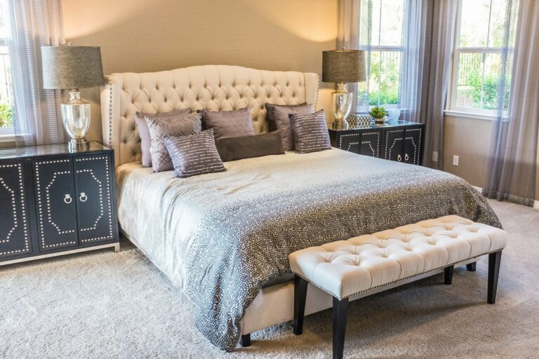 Schlafkomfort im Eigenheim planen: Härtegrad, Kern und Größe systematisch vergleichen A tufted headboard bed with grey patterned bedding and a cream bench in a bedroom