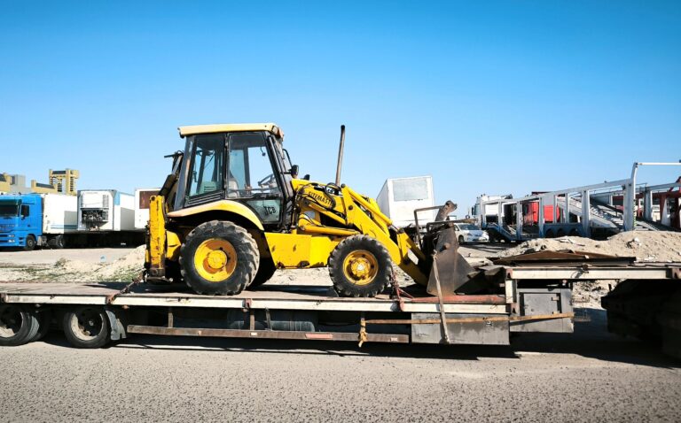 Maschinentransporte – Minibagger auf Tieflader vor der Baustelle